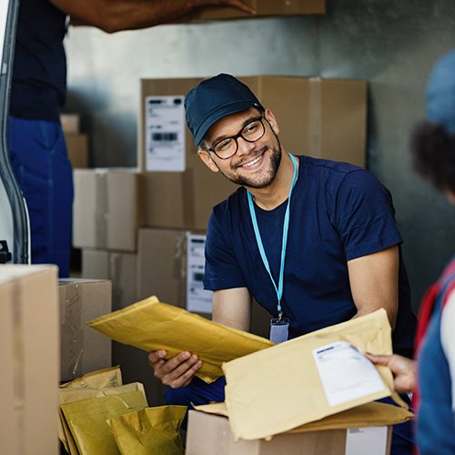 Young manual worker talking to his female colleague while sorting packages for shipment in a delivery van.