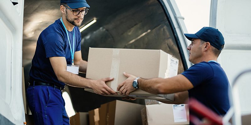 Delivery men loading carboard boxes in a van while getting ready for the shipment.