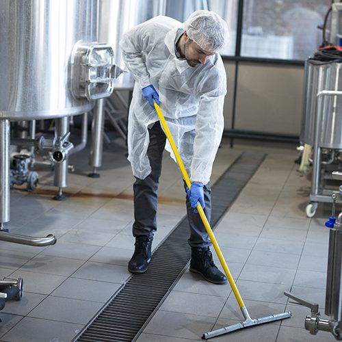 Professional cleaner wearing protection uniform cleaning floor of production plant.